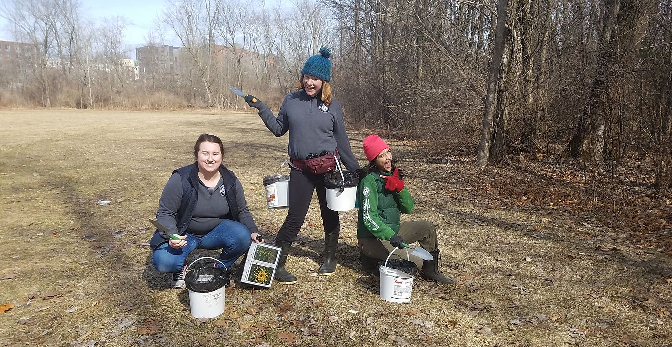 Three women posing with their buckets full of dog stool they have cleaned up.